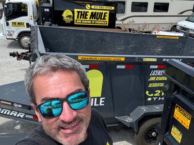 Man takes selfie wearing sunglasses and The Mule junk removal shirt near trailers and truck.