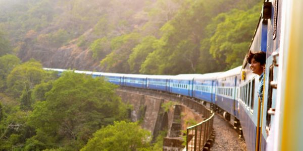 Person joyfully looking out from a train crossing a scenic bridge surrounded by greenery.