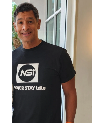 Smiling man wearing a black 'Never Stay Idle' T-shirt.