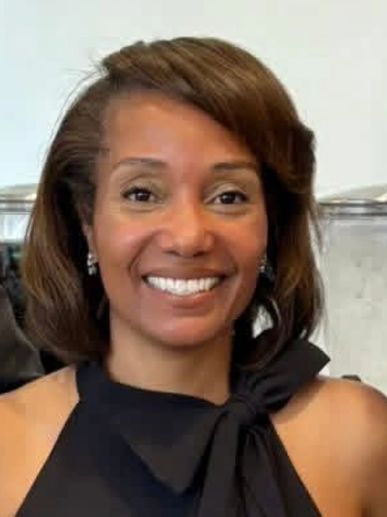Smiling woman in a black dress with a bow detail.