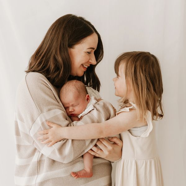 Baby sleep consultant holding newborn baby and smiling at toddler in beige and white tones