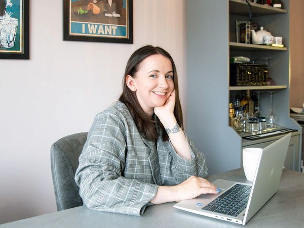Smiling baby sleep consultant working on a laptop at a desk in a cozy room, giving parenting support with sleep training.