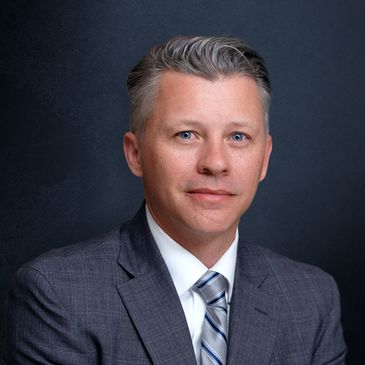 Professional man in a suit with a striped tie posing against a dark background.