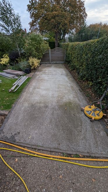 Concrete driveway with cleaning equipment and garden surroundings.
