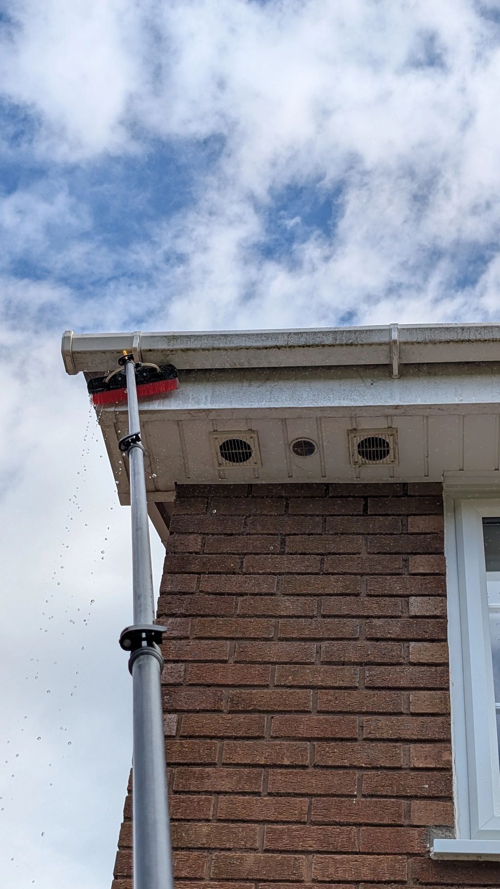 Cleaning gutters using a long brush and water supply.