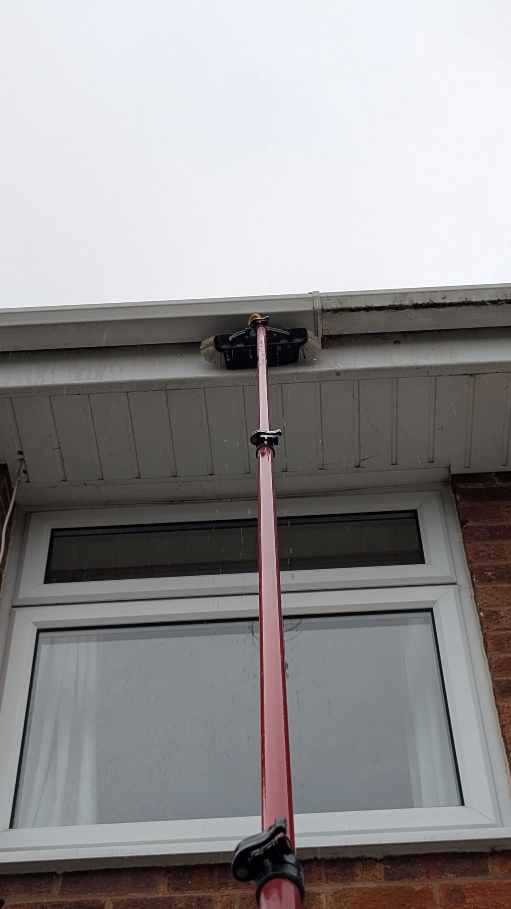 Cleaning a house gutter with a long brush.