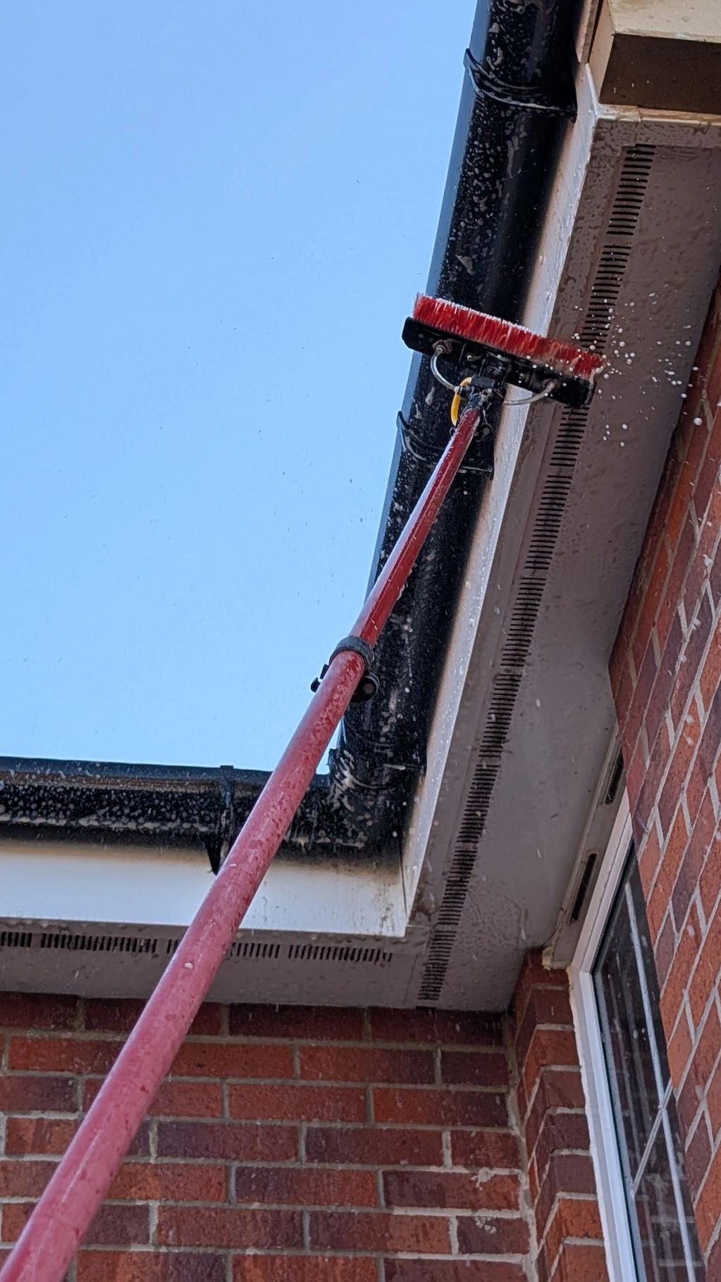 Long brush cleaning gutters with water spray.