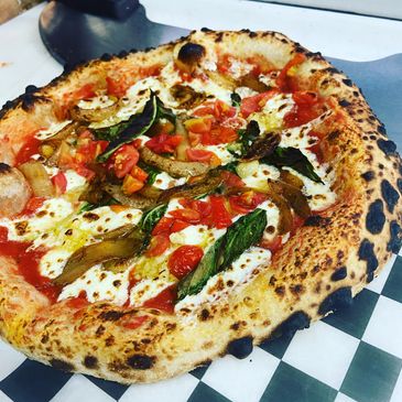 Neapolitan-style pizza with fresh mozzarella, basil, tomatoes, and roasted vegetables.