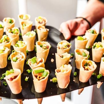 Mini spring rolls filled with fresh vegetables served on a black tray.