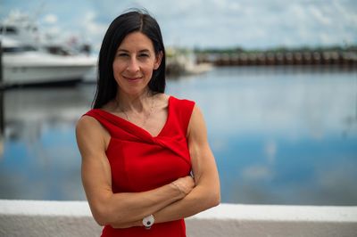 Confident woman in a red dress standing by the waterfront with arms crossed.