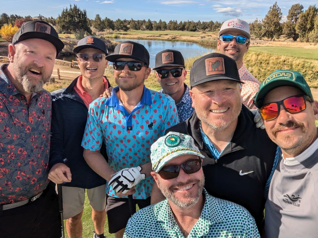 Eight men smiling on a golf course on a sunny day.