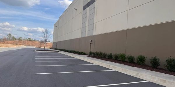 Empty parking lot beside a large beige and brown building on a clear day.