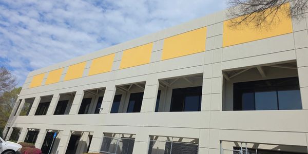 Modern two-story office building with yellow accents and large windows under a blue sky.