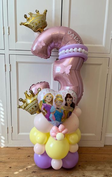 A pink number 3 balloon with princess-themed decorations and crowns.