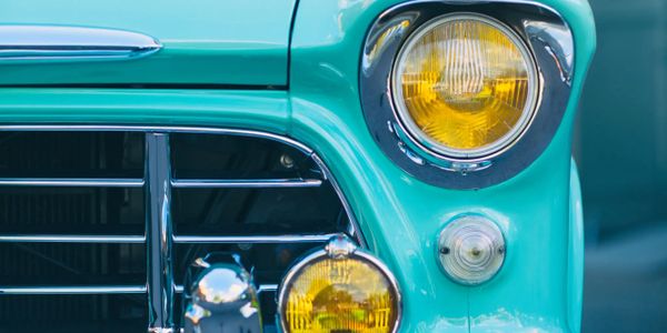 Close-up of a vintage car's front with turquoise paint and yellow headlights.