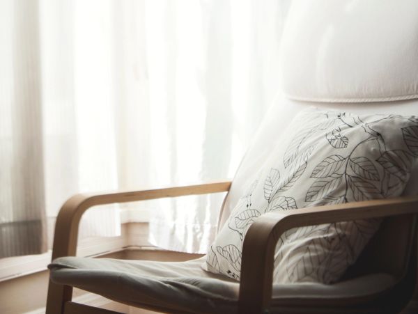Cozy chair with a leafy patterned cushion near bright curtains.