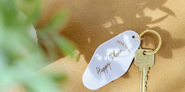 A key with a tag saying 'Keys to my Happy Place' on a sunlit surface.