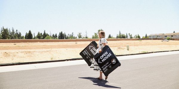 Woman walking on road carrying two open house signs for real estate.