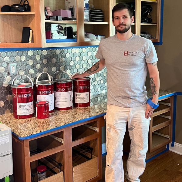 Man stands next to red paint cans on a kitchen countertop with hexagonal tile backsplash.