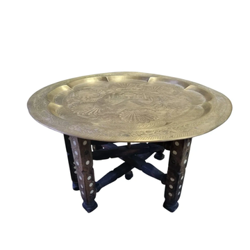 Mesa artesanal con tapa de latón y patas de madera tallada.