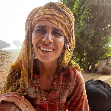 A smiling woman in traditional attire sitting outdoors near a black dog.