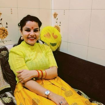 A woman in a yellow outfit smiles while sitting on a couch with floral tiles behind her.