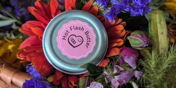 A tin of Hot Flash Butter surrounded by colorful flowers.