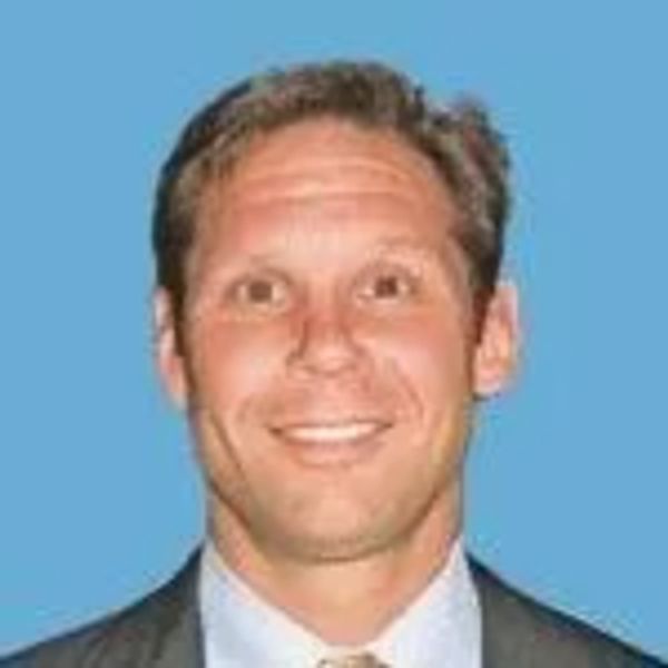 Smiling man in business attire against blue background.