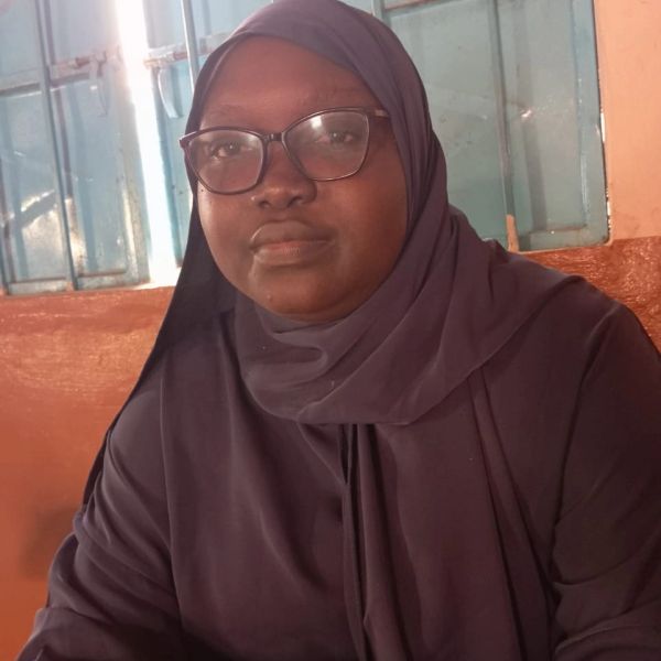 Woman in a dark hijab and glasses sitting indoors.