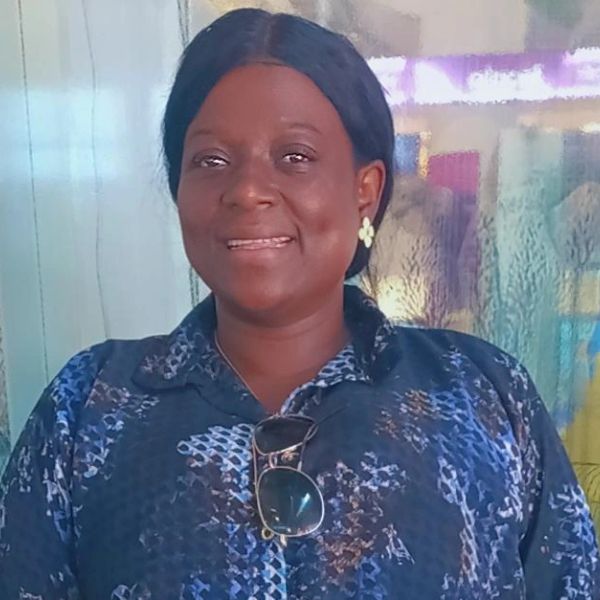 Woman smiling wearing a blue patterned shirt and earrings.
