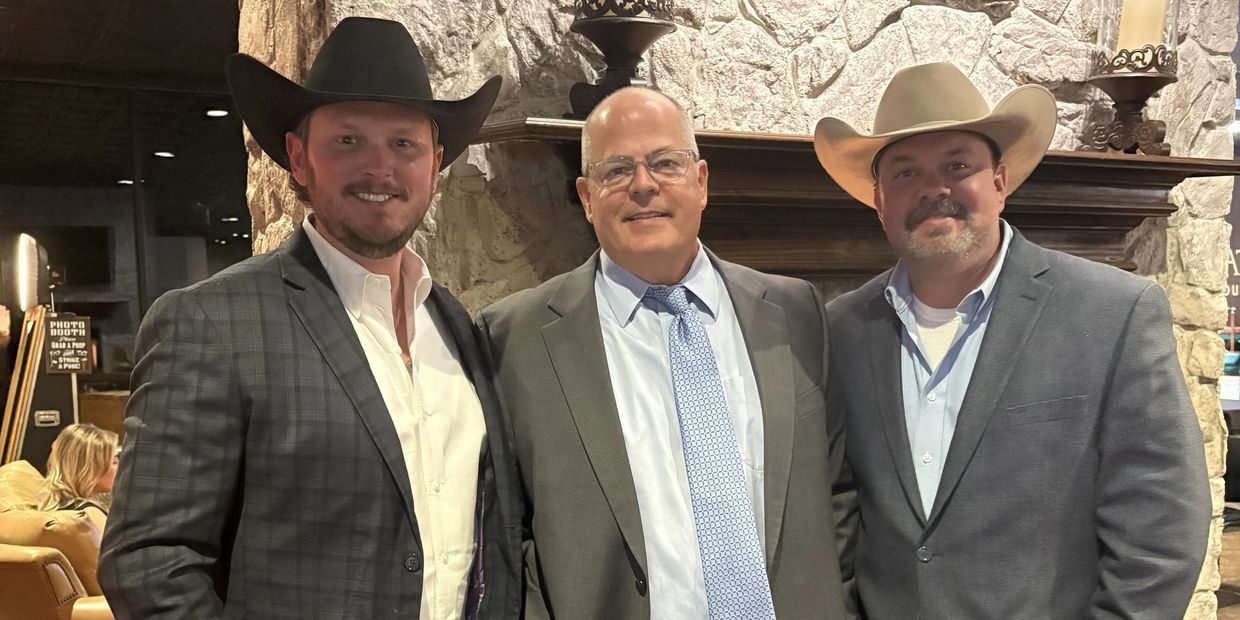 Three men in suits and cowboy hats smiling indoors.