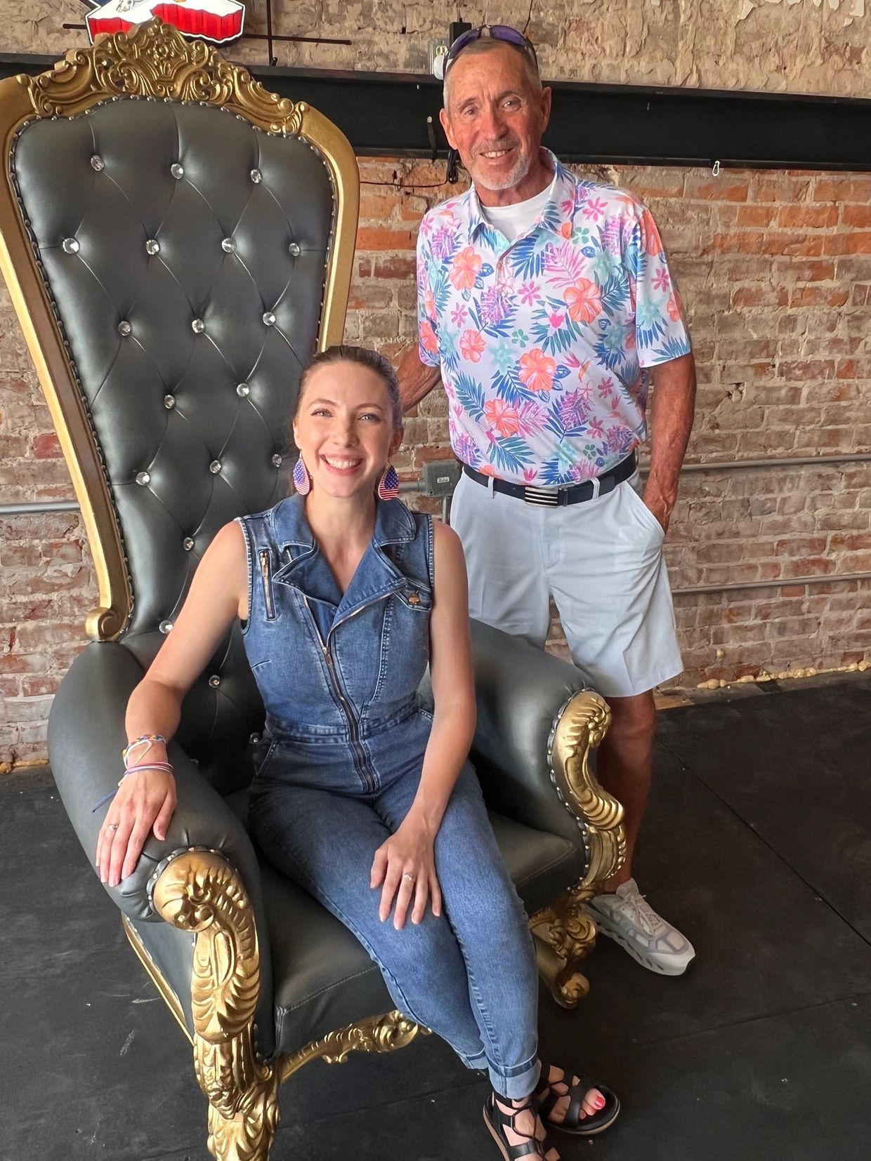 Smiling woman sitting on an ornate chair with a man standing beside her.