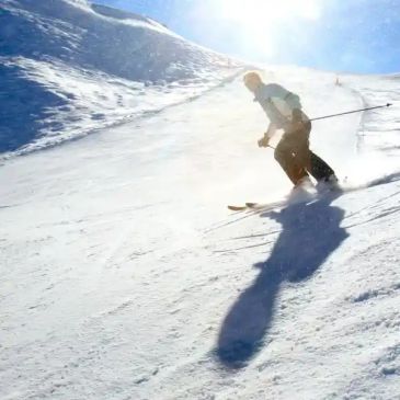 Skier descending a snowy slope under bright sunlight