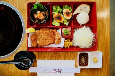 Japanese bento box meal with fried cutlet and side dishes.