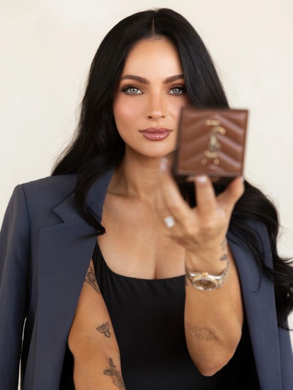 Woman with dark hair holding a small brown wallet.