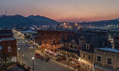 Small town street at dusk with lights and mountains in the background.
