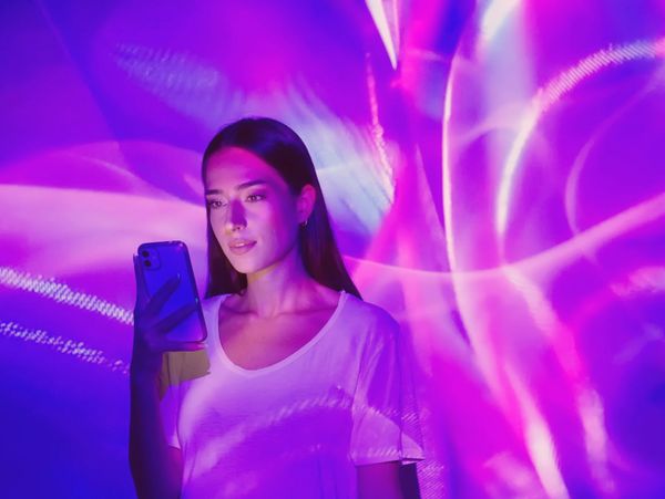 Woman using smartphone with vibrant purple and pink light projections.