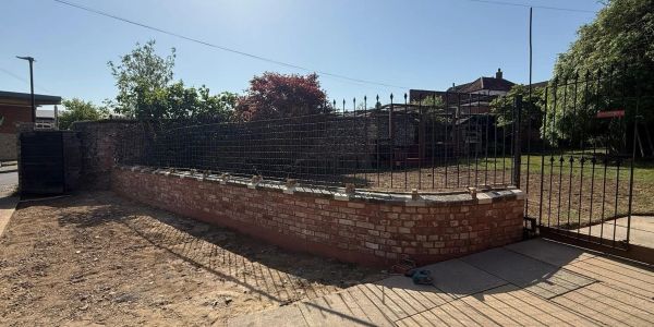 Newly built brick and iron fence around a garden.