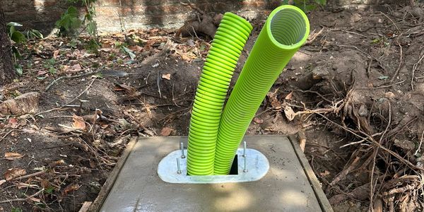 Green corrugated pipes emerging from concrete base outdoors.