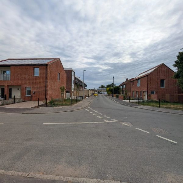 Residential street with brick houses under cloudy sky.
