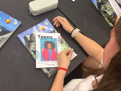 Person reading a Teens magazine with other magazines on the table.