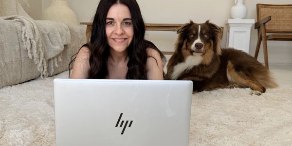 Woman with dog using laptop on a carpet.