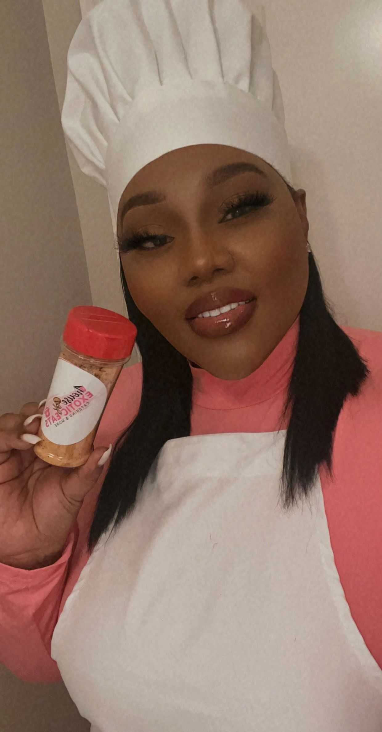 Woman in chef hat holding seasoning bottle.