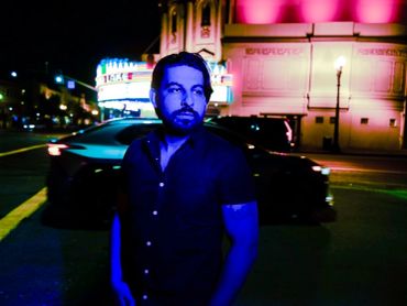 Man illuminated by blue light on a city street at night.