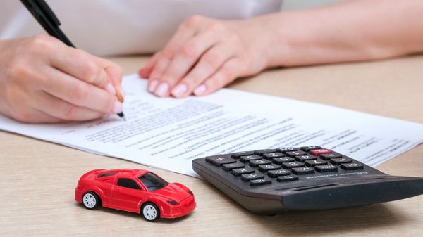 A person writes on a document alongside a calculator and a toy red car
