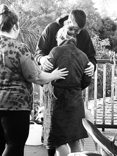 Three people sharing a comforting hug outdoors on a porch.