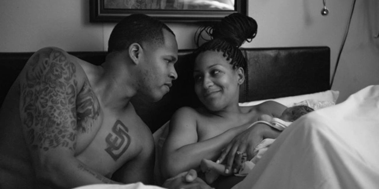 A couple lovingly gazes at each other while holding their newborn baby in bed.