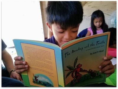 A boy intently reading a book titled The Monkey and the Turtle.