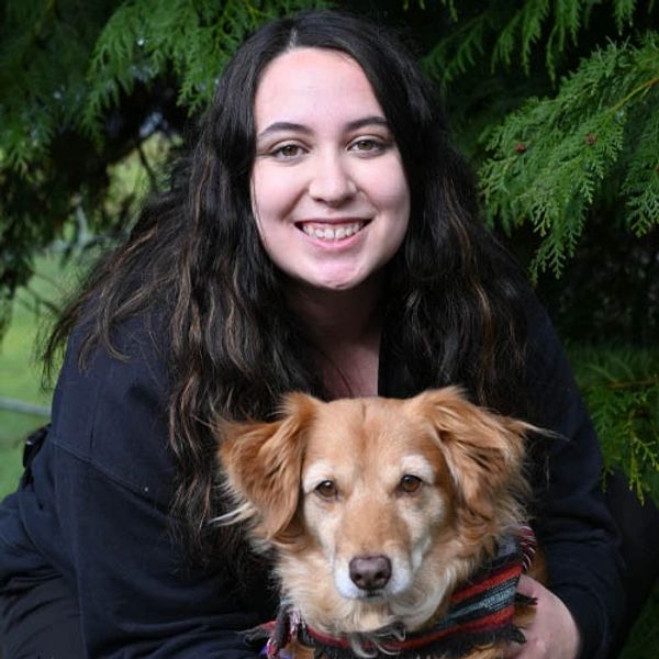 A smiling woman with long dark hair holding a golden-brown dog outdoors.