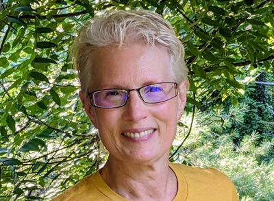 Smiling woman with glasses in a yellow shirt outdoors.